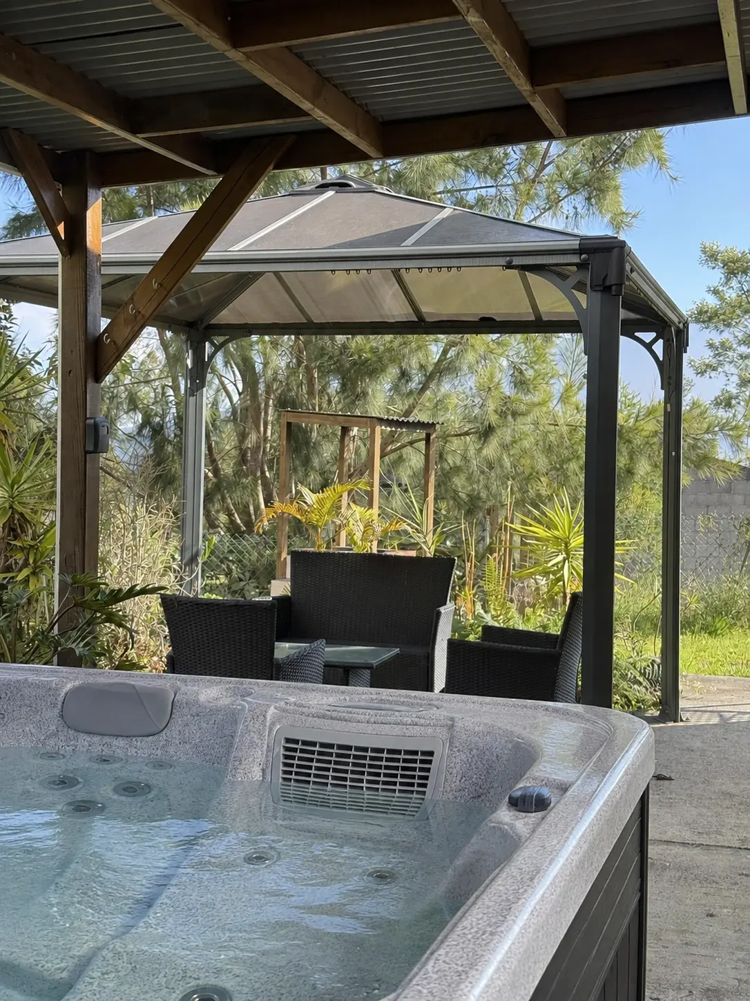 Vue depuis le jacuzzi de La Caz'à Chisy sur le gazebo, le salon en résine tressée et le jardin tropical