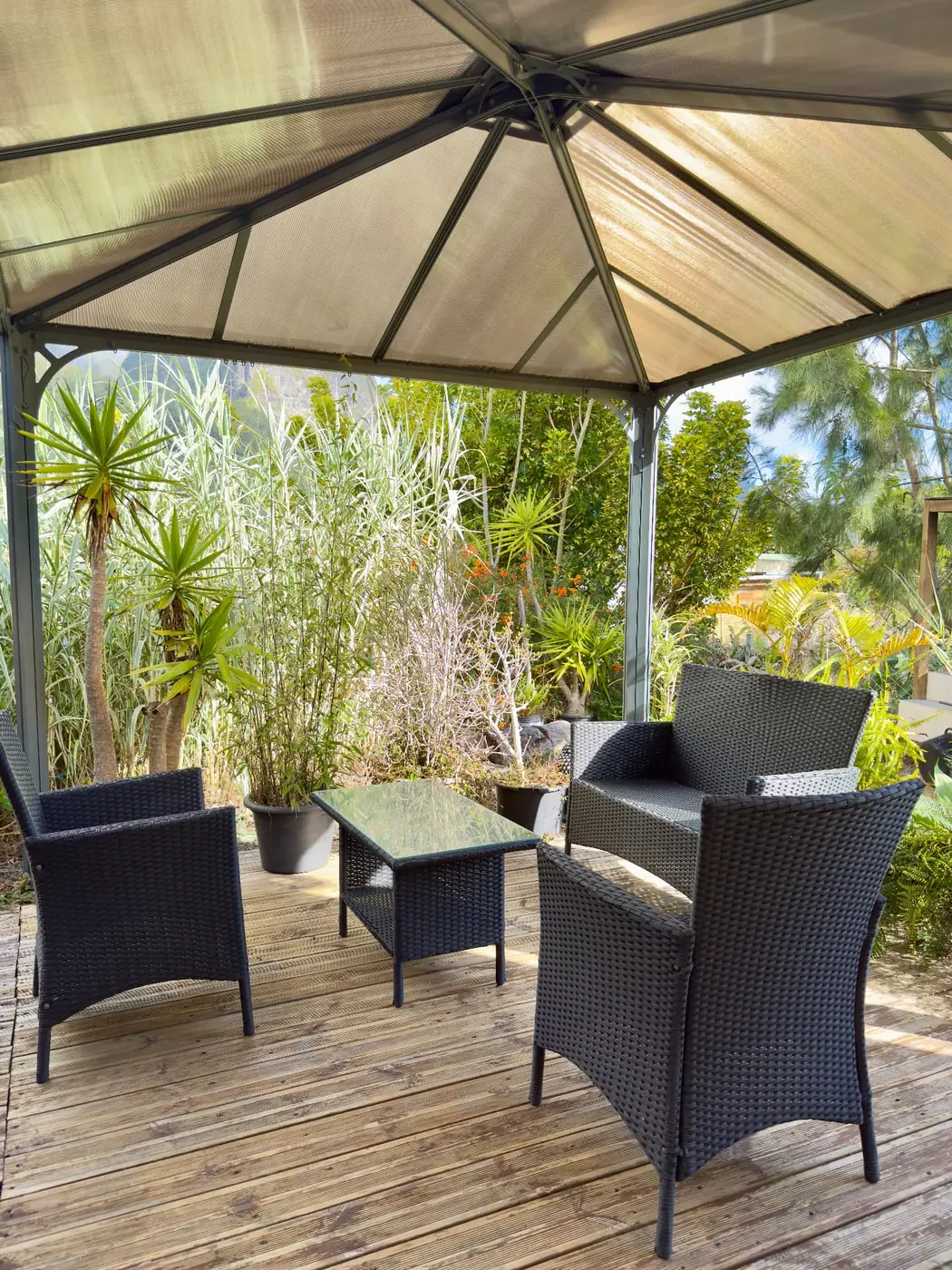 Terrasse couverte de La Caz'à Chisy à Bras-Sec avec salon de jardin en résine tressée entouré de végétation