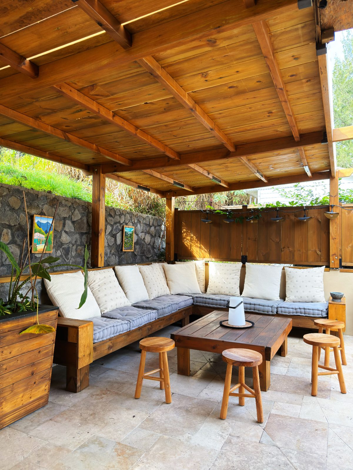 Salon extérieur couvert du Chalet Des Sens à Cilaos de jour, banquette d'angle et table basse sous pergola en bois