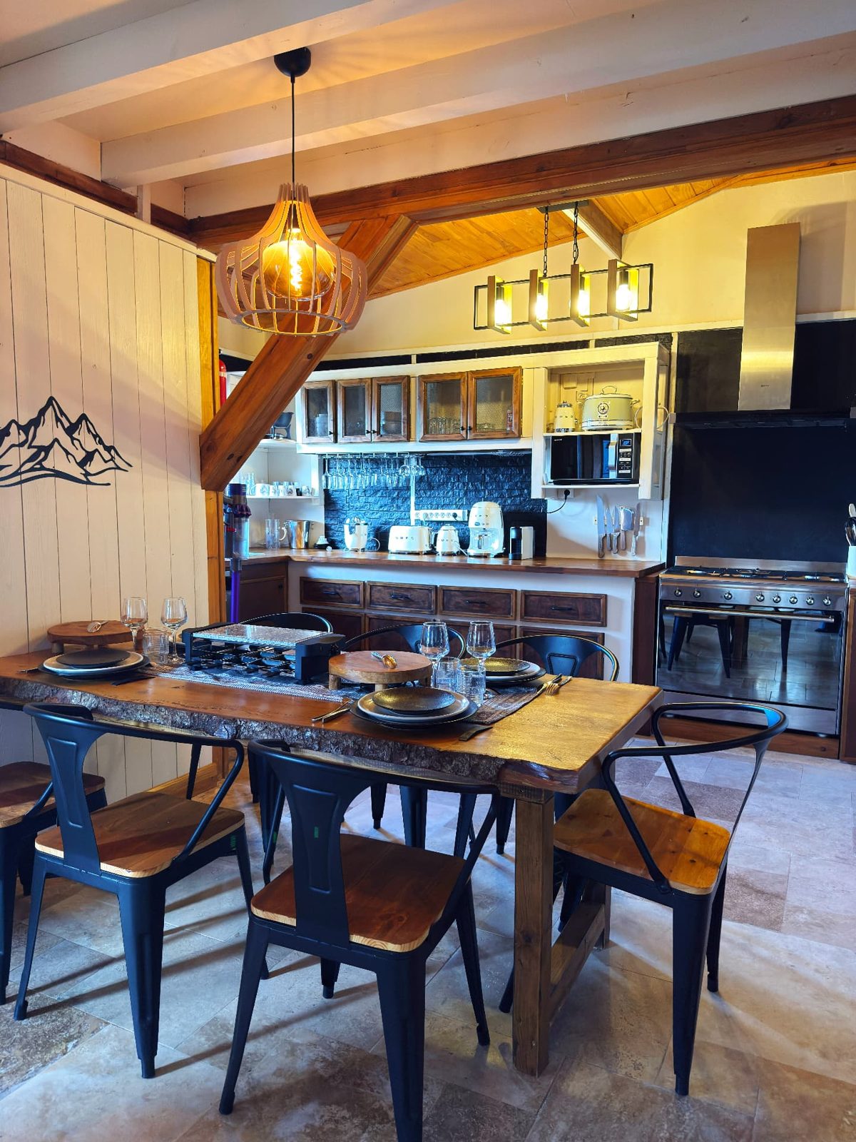 Salle à manger du Chalet Des Sens à Cilaos avec grande table en bois brut, appareil à raclette et charpente apparente